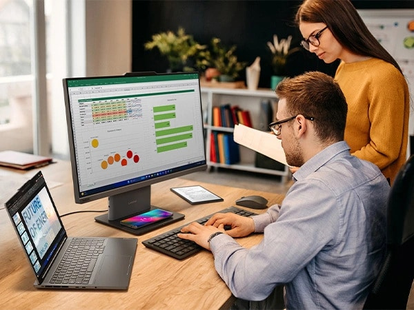 Two people at a desk using a Lenovo laptop and wireless keyboard and mouse to work with data on a Lenovo ThinkCentre Neo 50a Gen 5 24 inch Intel monitor