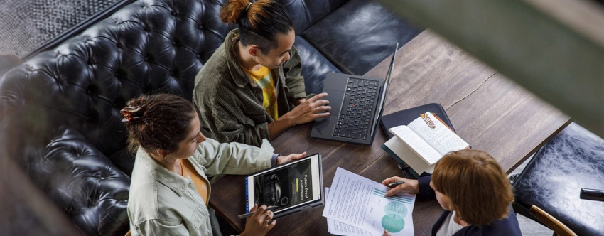 Overhead shot of three people sitting around a table, with each one working. Two are using Lenovo ThinkPad X1 2-in-1 Gen 9 convertible laptops, with one typing and one using the included Lenovo Slim Pen.