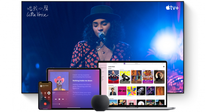 大型電視螢幕上有一個女士唱歌。一部 MacBook Pro、一部 iPad，一部 iPhone及一部太空灰 HomePod mini 排列在前方。