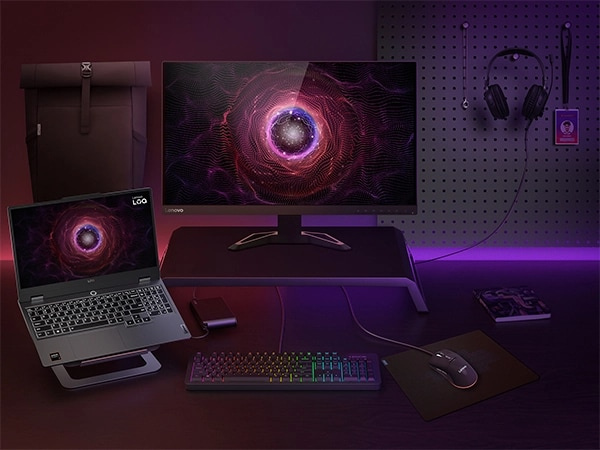 The Lenovo LOQ 15AHP9 laptop on a stand, surrounded by accessories including a monitor, keyboard, mouse, and headset